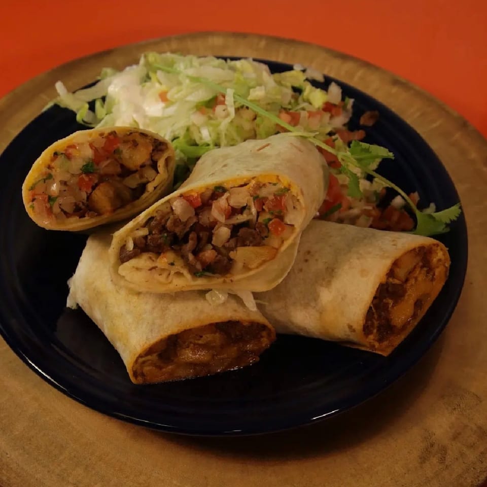 Three burritos, one cut in half, revealing a savory filling, served with a side salad.