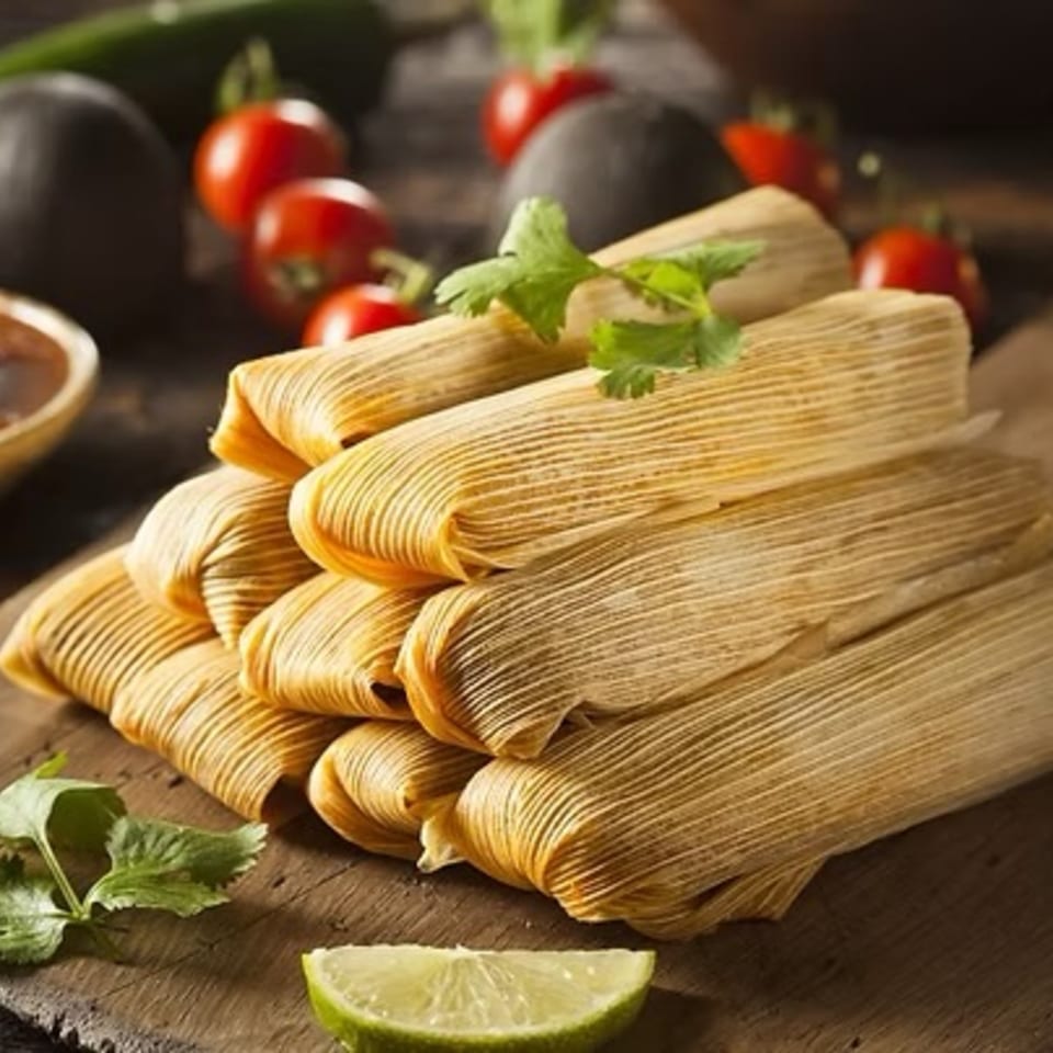A stack of tamales wrapped in corn husks, garnished with cilantro and a lime wedge.