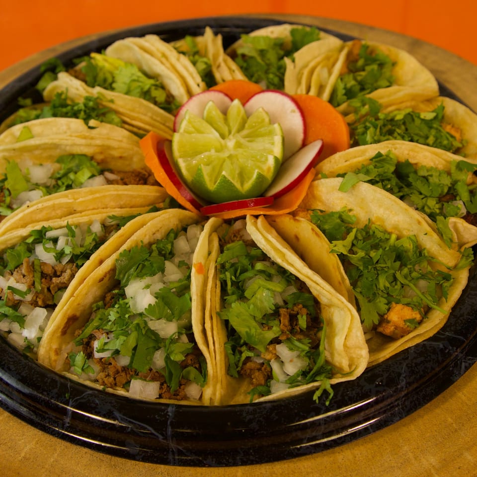 A platter of Que Pasa Tacos with various fillings, cilantro, onions, and a lime garnish.
